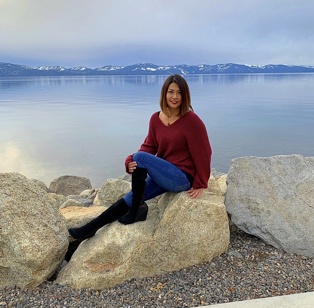 Ikumi in a burgundy sweater seated on rocks at the shore of Lake Tahoe